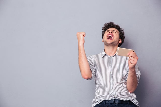 Happy man holding smartphone and celebrating his success over gray background