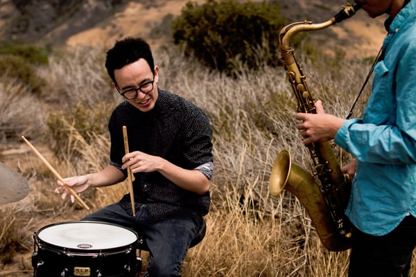 In a field outdoors person wearing glasses drums on the left and someone plays saxaphone on the righ.jpg