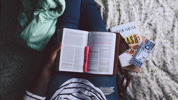 a_person_with_tattoos_sits_reading_a_book_with_highlighters_nearby.jpg