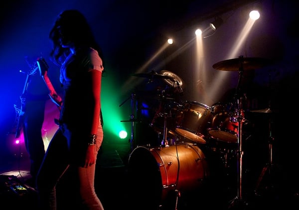 A musician stands onstage in front of a drum kit at a concert.