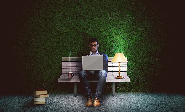 A man sits on a bench typing on laptop in his lap.jpg